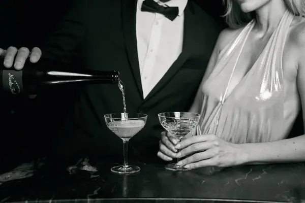 Ein Mann im Anzug und eine Frau im Kleid sitzen an einer Bar mit Weingläsern.
