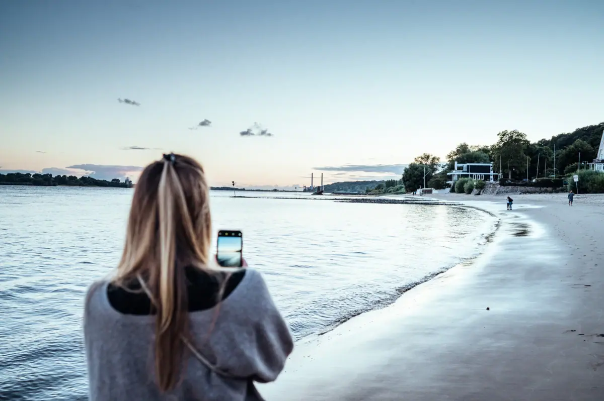 Eine Frau fotografiert den Elbstrand in Hamburg.