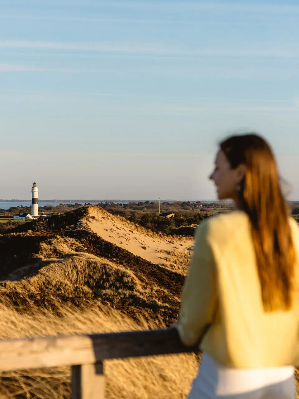Eine Frau steht auf einem Zaun und blickt auf einen Leuchtturm auf Sylt.
