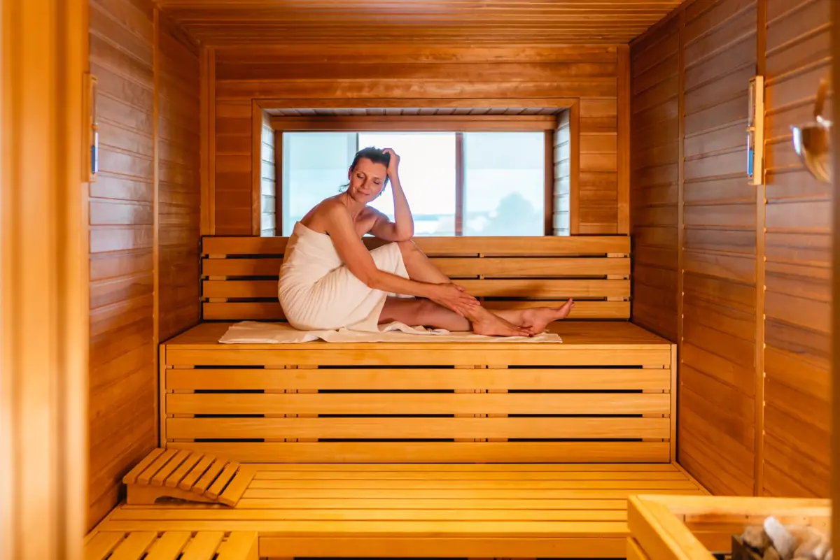 Eine Frau in einem Handtuch sitzt auf einer Holzbank in einer Sauna.
