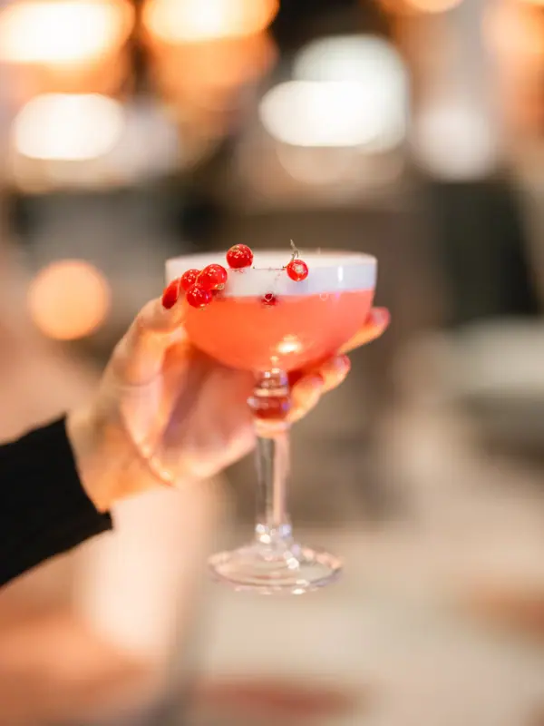 Eine Hand hält ein Glas mit rosa Flüssigkeit.