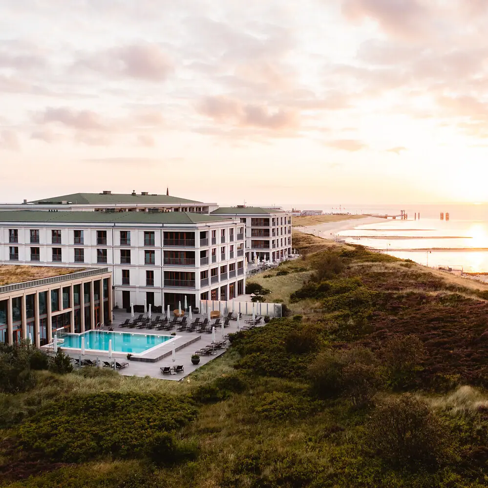 Das A-ROSA Sylt mit einem Outdoor-Pool an den Dünen mit der Nordsee daneben..