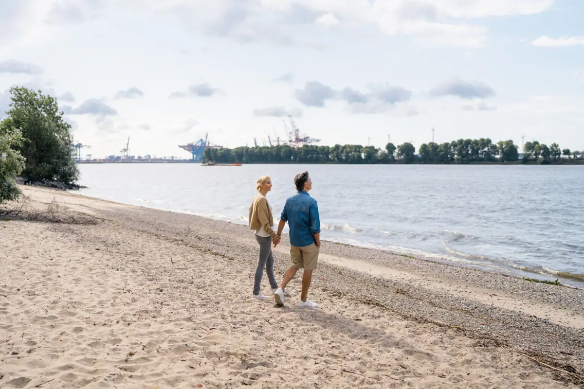 Ein Mann und eine Frau halten sich an den Händen am Strand.