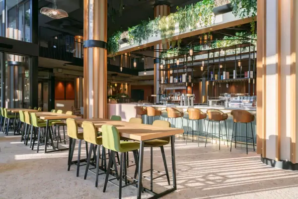 Die Bar im A-ROSA Gardasee mit großen Säulen, einer langen Theke sowie Tischen und Stühlen.
