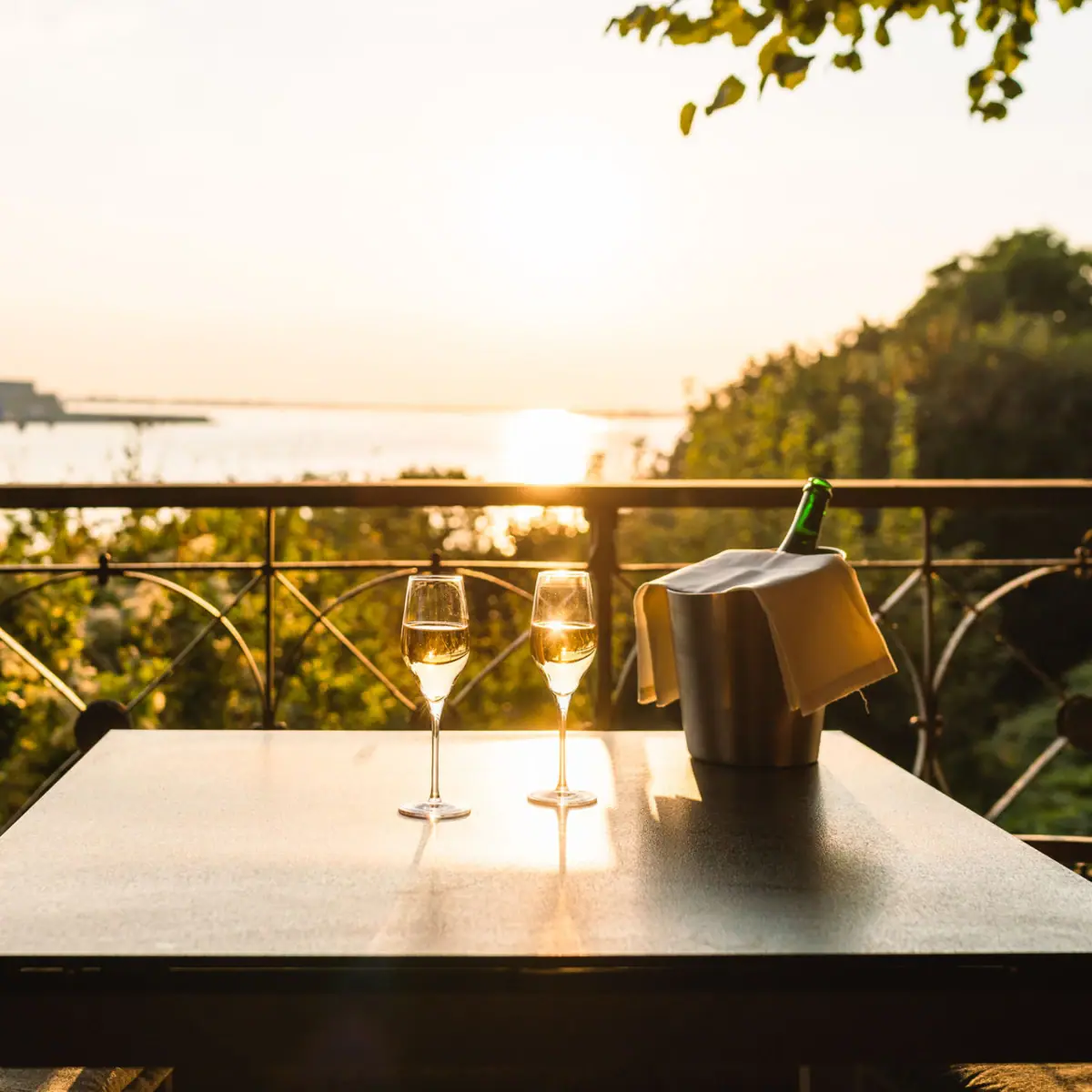 Ein Tisch mit Weingläsern auf der und einem Weinkühler darauf auf der Lindenterrasse in Hamburg mit Elbblick.