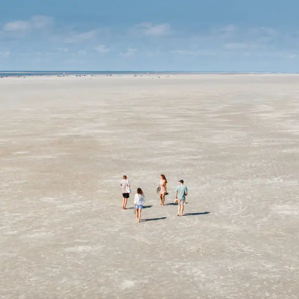 Eine Gruppe von Menschen läuft am Strand von St. Peter-Ording beim Urlaub am Wattenmeer.