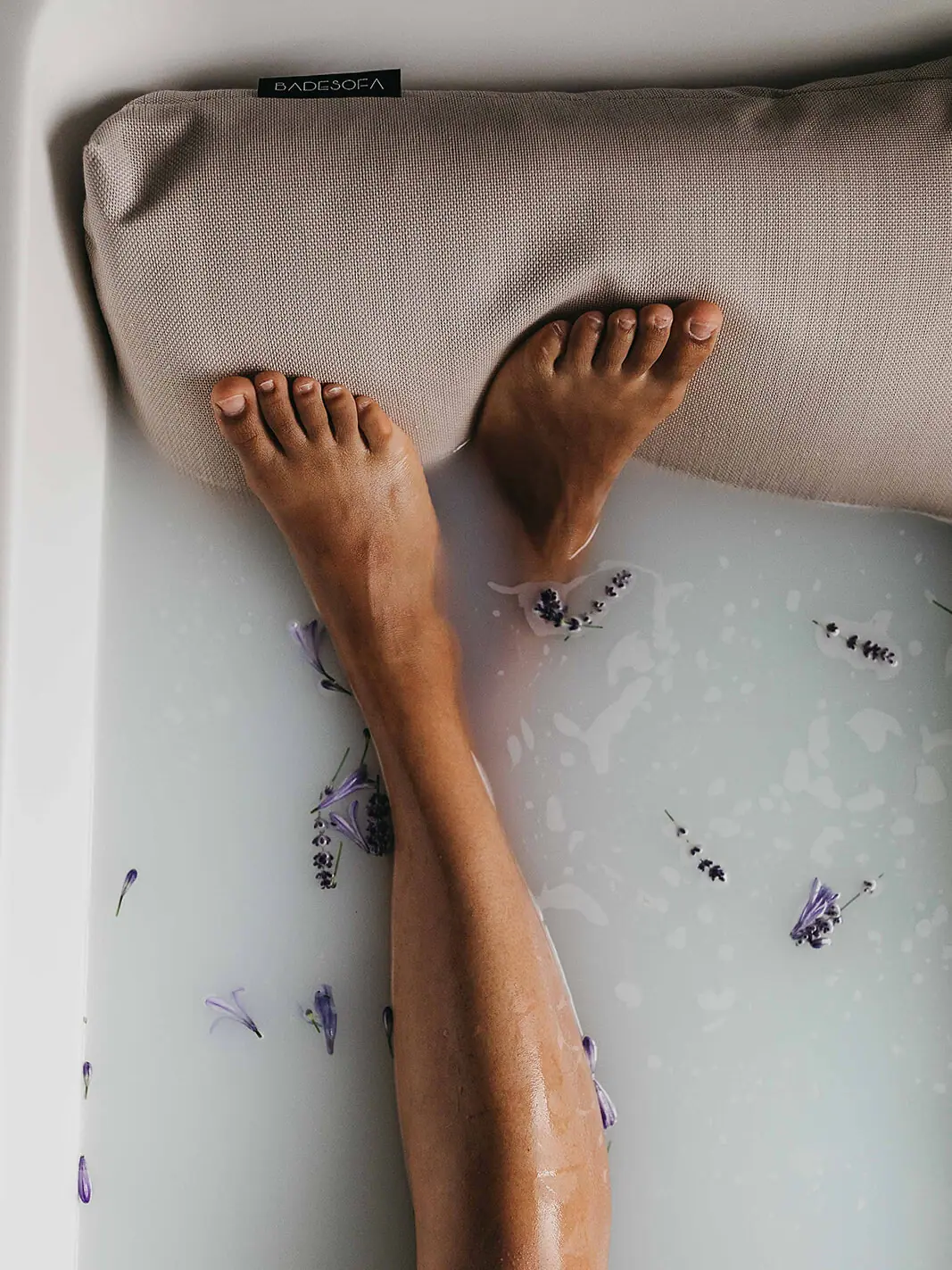 Füße einer Person in einer Badewanne mit Milch und Blumen