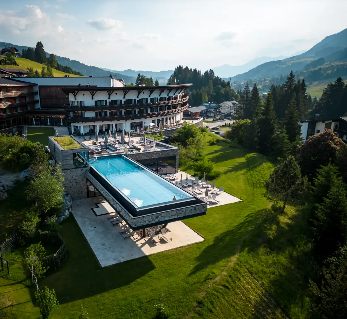 Ein Swimmingpool im A-ROSA Ifen Hotel Kleinwalsertal, umgeben von Bäumen und klarem Himmel.