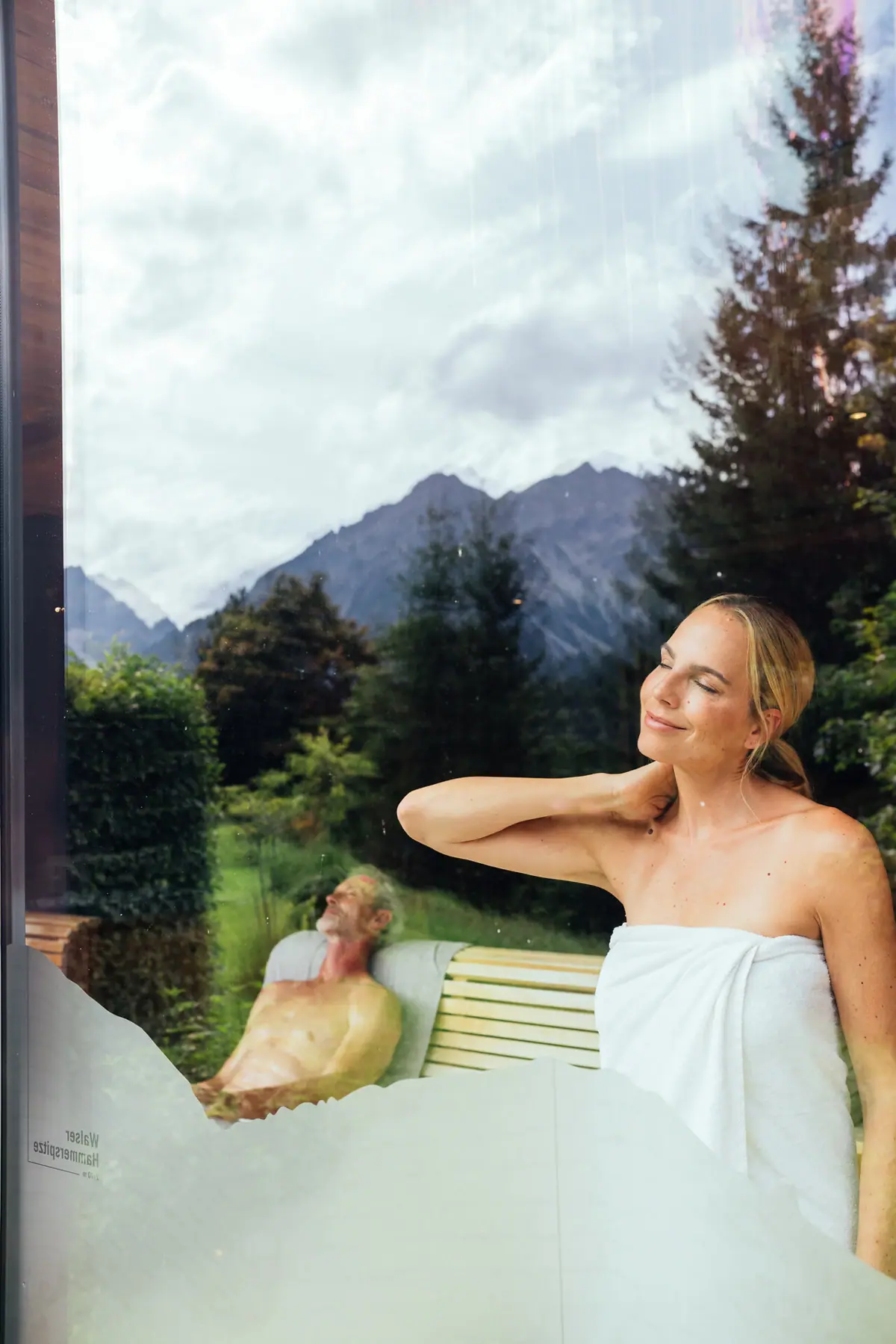 Eine Frau schaut aus dem Fenster einer Panoramasauna, in dem sich der Ausblick spiegelt.