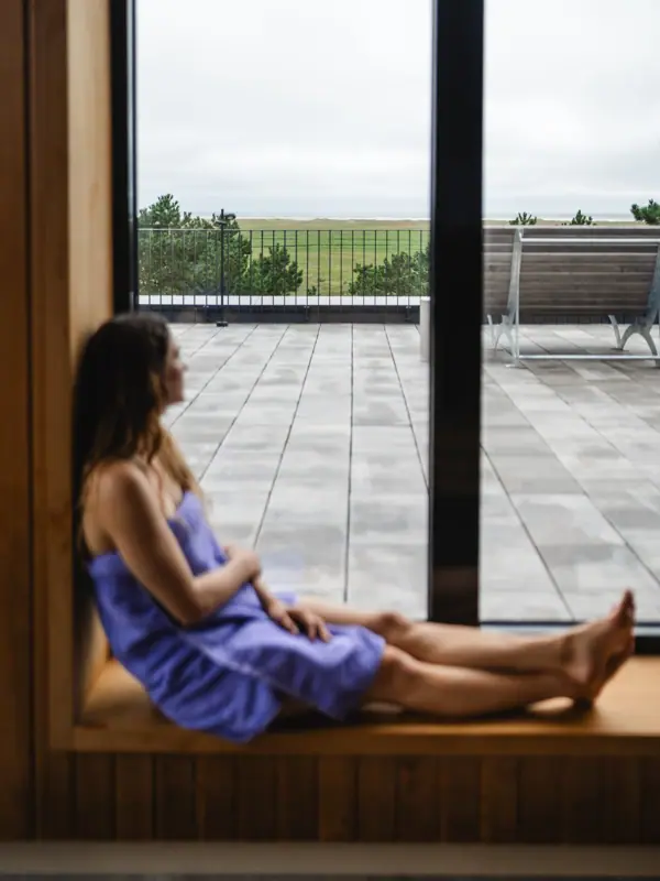 Frau sitzt auf einer Fensterbank in der Sauna vom Urban Nature Hotel St. Peter-Ording und schaut aus dem Fenster.