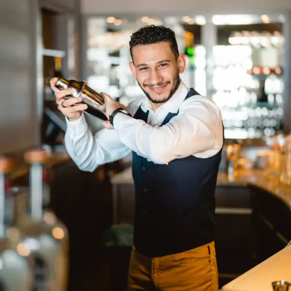 Ein Barkeeper in einer Hotelbar hält einen Shaker.