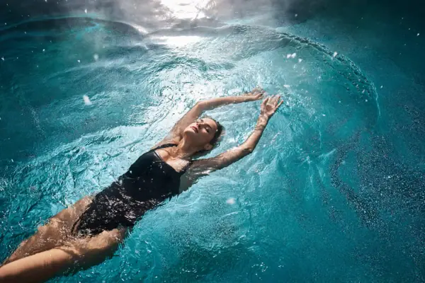 Eine Frau in einem schwarzen Badeanzug treibt in einem Pool.