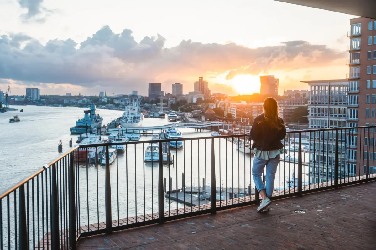 Eine Frau steht auf der Elbphilharmonie Plaza und blickt auf die Elbe mit Booten im Hintergrund.