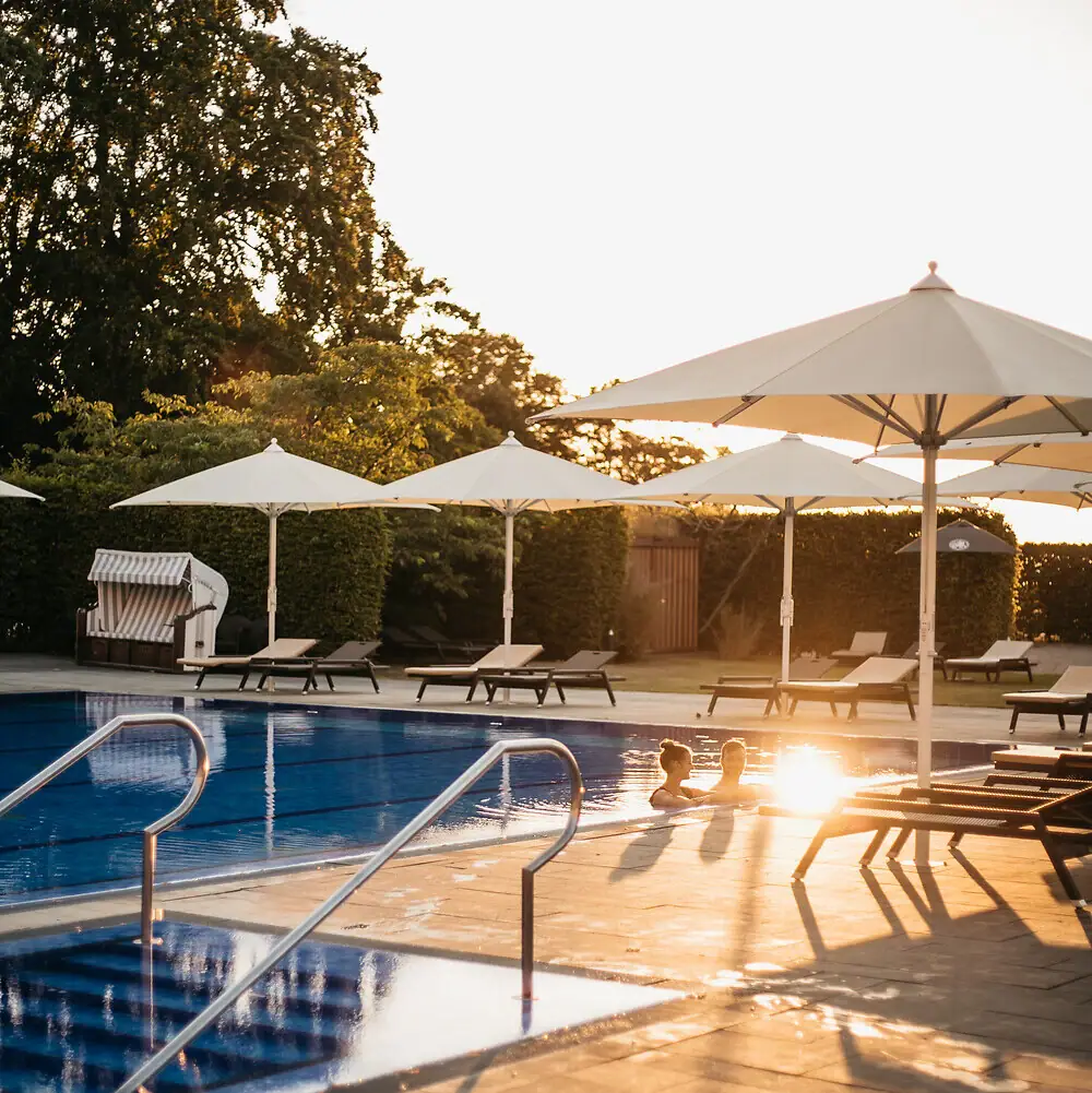 Eine Person im Pool mit Sonnenschirmen und Stühlen.