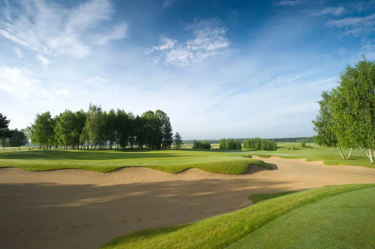 Ein Sandbunker auf einem Golfplatz mit grüner Umgebung und blauem Himmel.