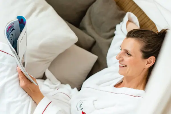 Eine Frau im Bademantel liegt auf einer Liege und liest.