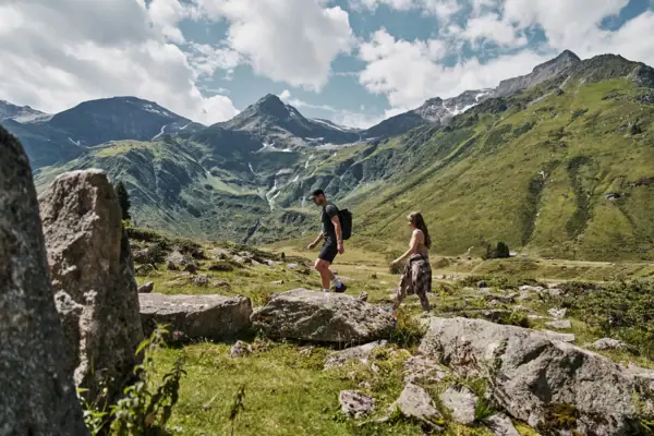Ein Mann und eine Frau wandern auf einem felsigen Hügel mit Bergen im Hintergrund.