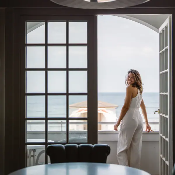 Eine Frau steht auf einem Balkon im A-ROSA Kurhaus Binz mit Blick auf die Ostsee und lächelt.