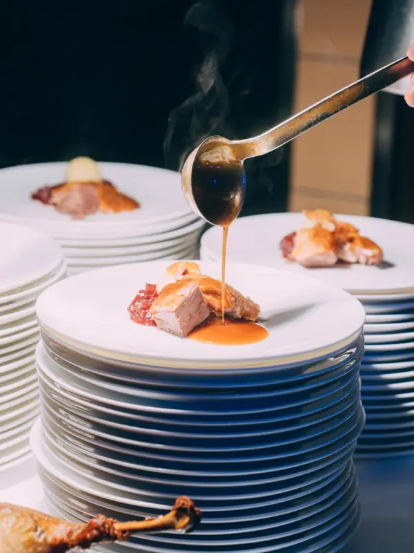 Eine Person gießt Sauce über einen Teller mit Essen.