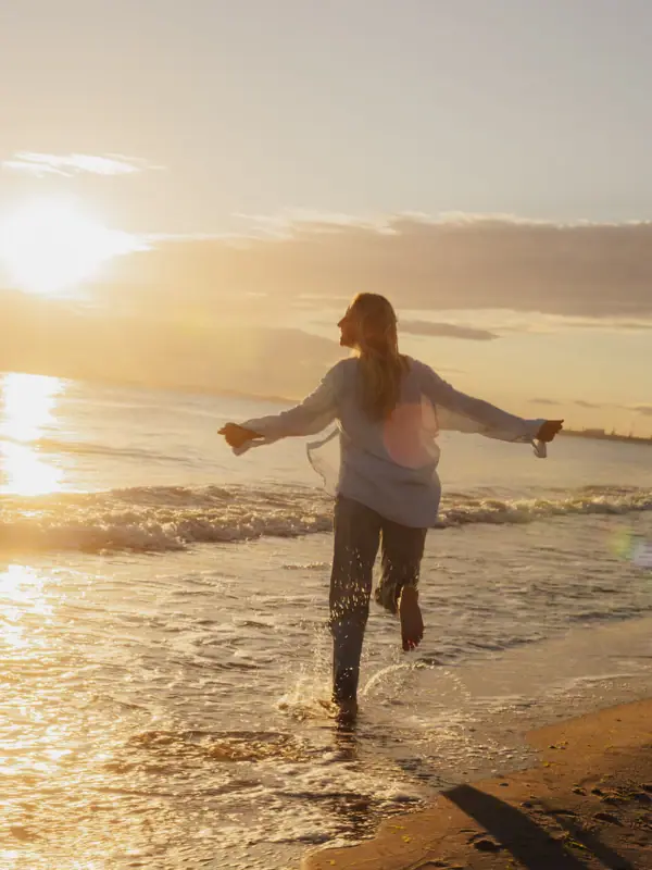 Eine Frau läuft bei Sonnenaufgang am Strand der Ostsee entlang.